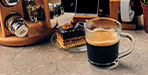 Taza de café de vidrio junto a una torta de chocolate