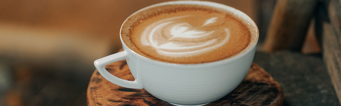 Taza blanca de café con diseño sobre la bebida, sobre mesa de madera